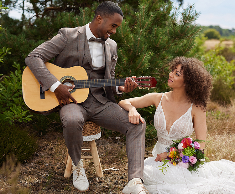Glückliches Brautpaar sitzt in der Natur. Bräutigam spielt Gitarre.