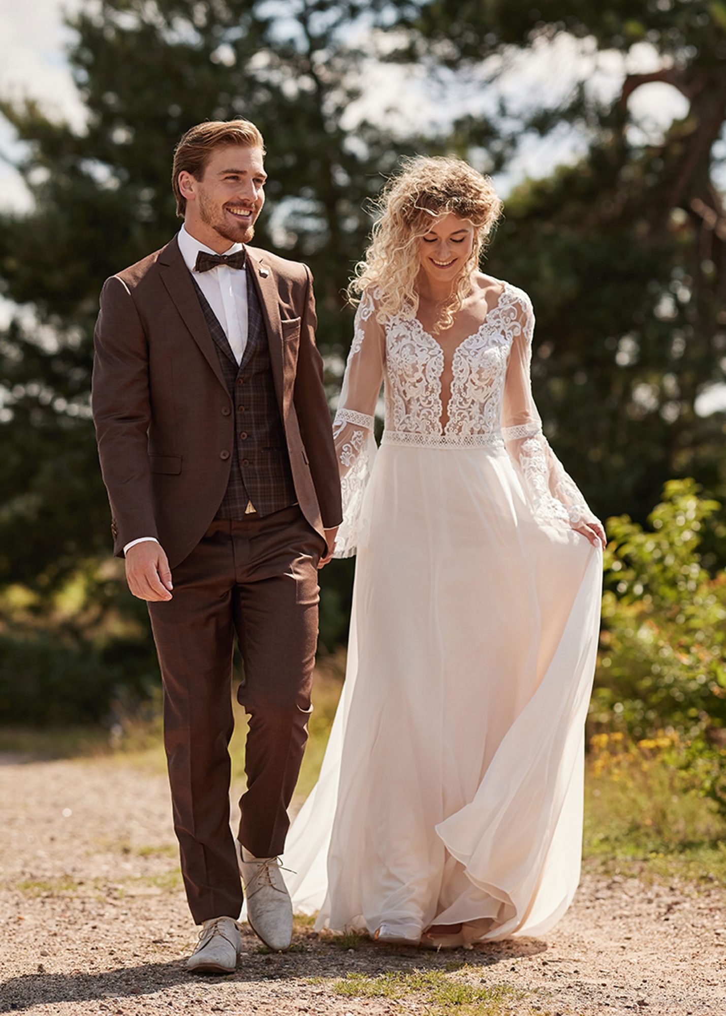 Glückliches Brautpaar spaziert. Mann trägt braunen Anzug von Immediate.
